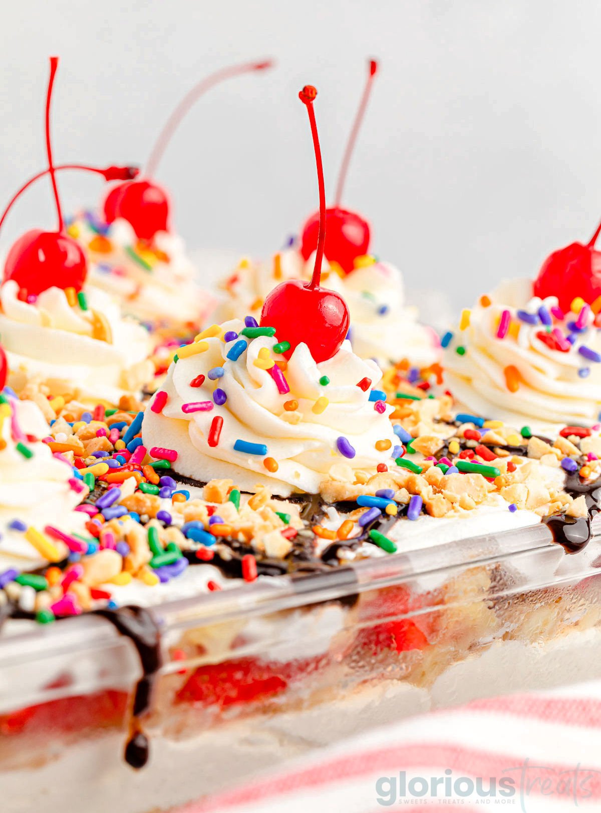 banana split dessert in a clear glass casserole dish. all the classic banana split toppings are on top of the dessert.