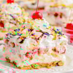 serving of no bake banana split dessert on white plate topped with whipped cream and a maraschino cherry.