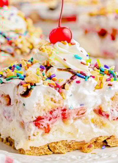 serving of no bake banana split dessert on white plate topped with whipped cream and a maraschino cherry.
