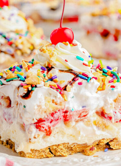 serving of no bake banana split dessert on white plate topped with whipped cream and a maraschino cherry.