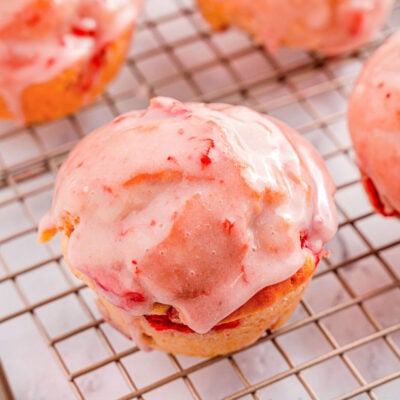 strawberry muffins on a wire rack.. One muffin is focused in on to show the texture of the strawberry glaze on top.