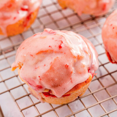 strawberry muffins on a wire rack.. One muffin is focused in on to show the texture of the strawberry glaze on top.