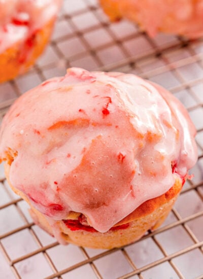 strawberry muffins on a wire rack.. One muffin is focused in on to show the texture of the strawberry glaze on top.