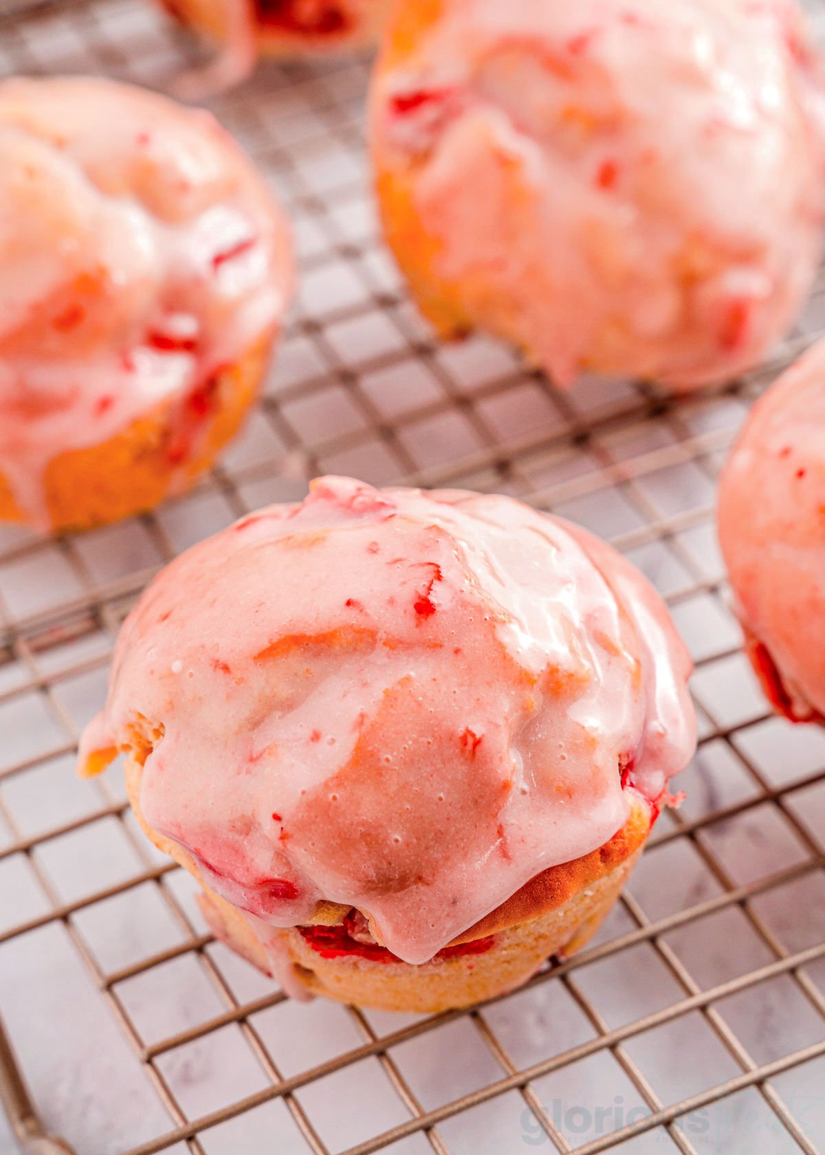 strawberry muffins on a wire rack.. One muffin is focused in on to show the texture of the strawberry glaze on top.