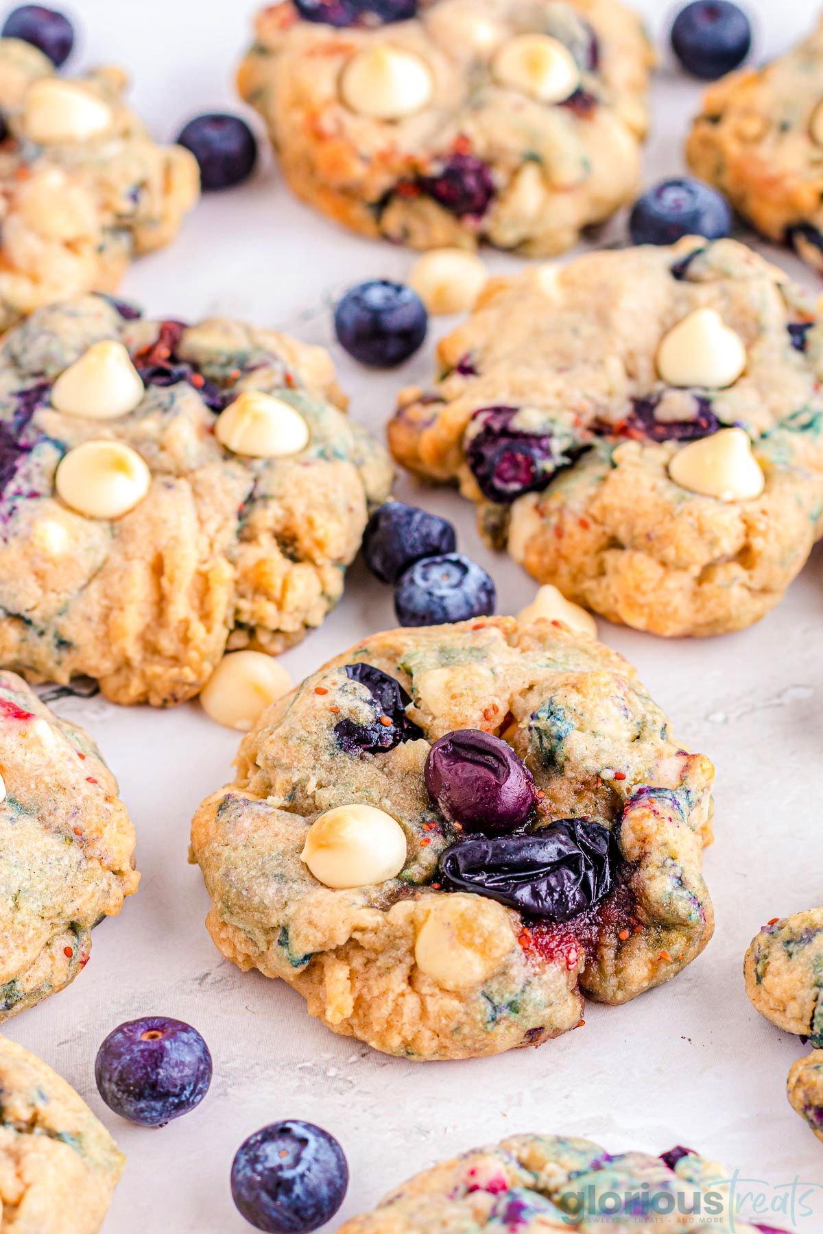 blueberry cookies on a white counter top. single fresh blueberries are scattered among the cookies.