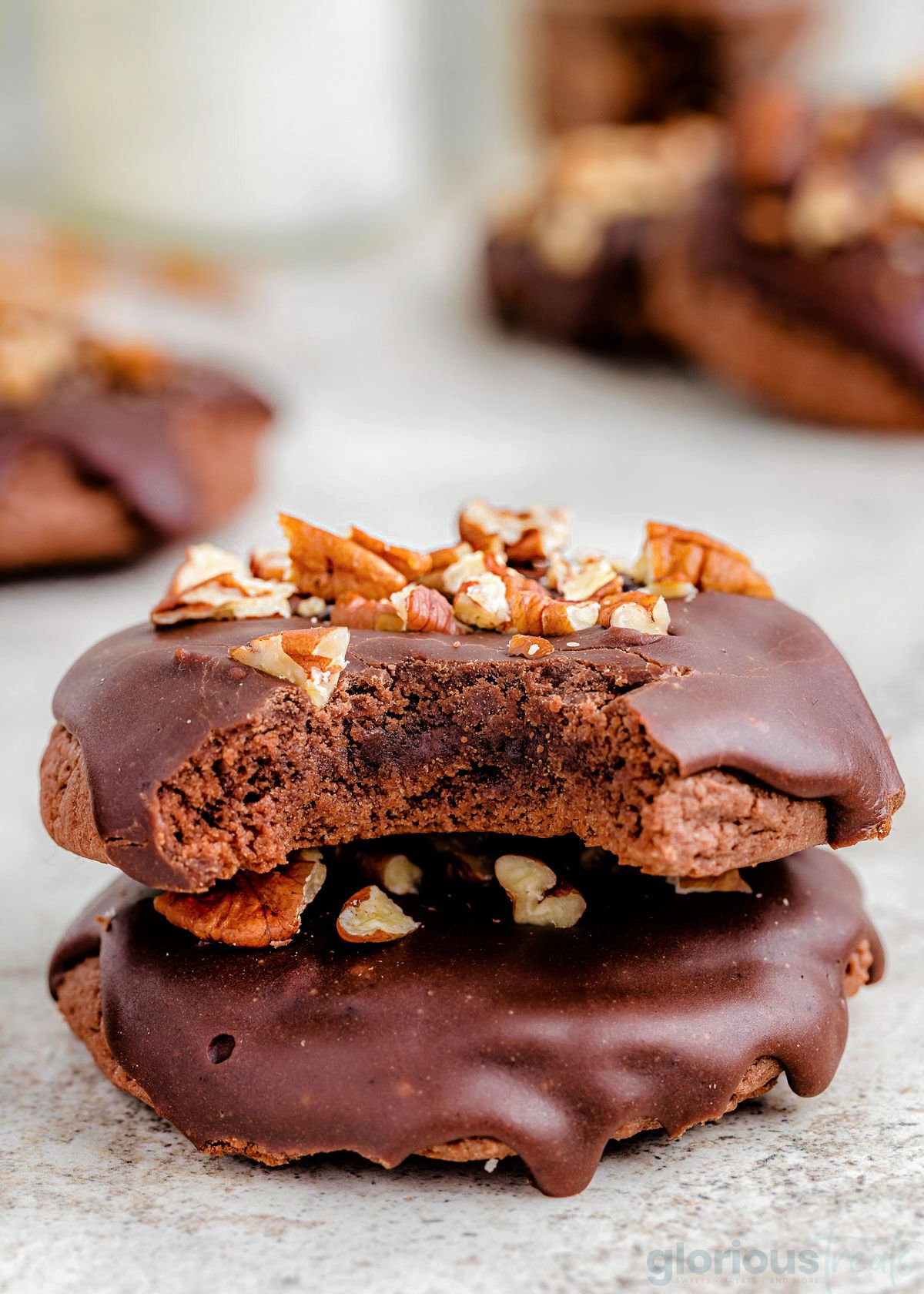 two chocolate cookies stacked on a white counter top. The top cookie has a bite taken out.