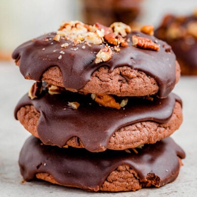 a stack of 3 chocolate cookies with chocolate drizzled on top and nuts sprinkled