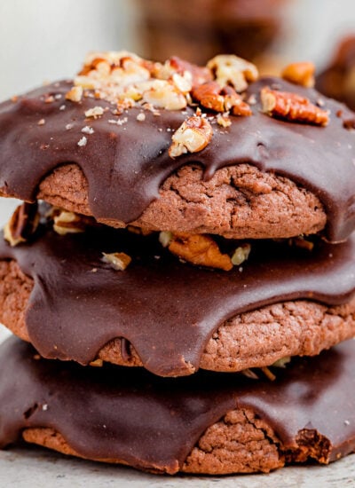 a stack of 3 chocolate cookies with chocolate drizzled on top and nuts sprinkled