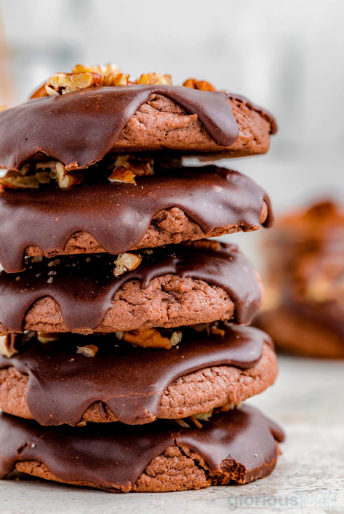 a stack of 5 chocolate cookies with chocolate icing on top and nuts sprinkled on the icing.