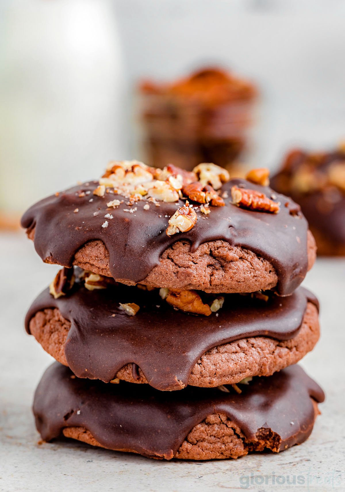 a stack of 3 chocolate cookies with chocolate drizzled on top and nuts sprinkled