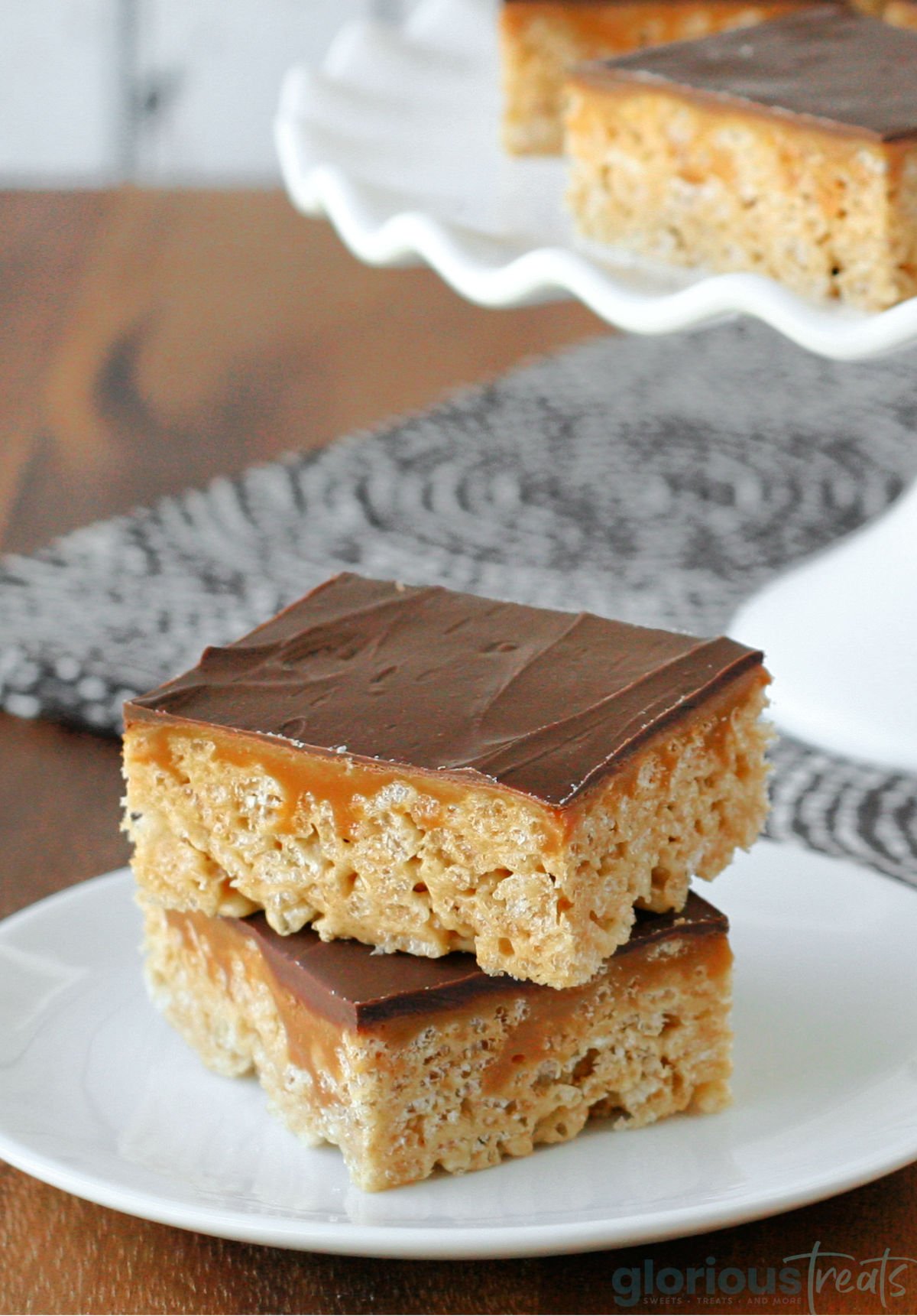 two whatcahmacallit krispie treats sitting on small nondescript white plate in front of cake stand with more treats.