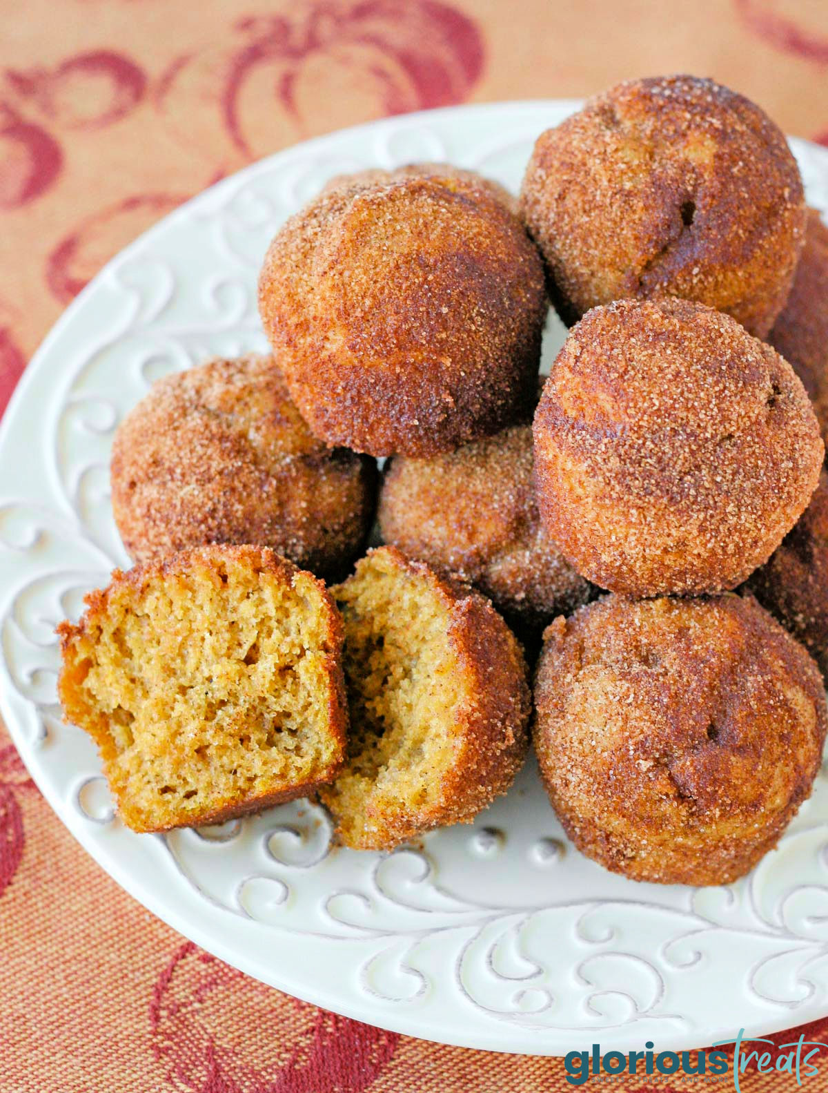 white plate filled with mini pumpkin muffins rolled in cinnamon sugar. one of the muffins has been torn in half.