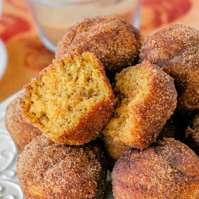 white metal pate is topped with a mound of pumpkin mini muffins rolled in cinnamon sugar so they look like donut holes. top muffin has been torn in half.