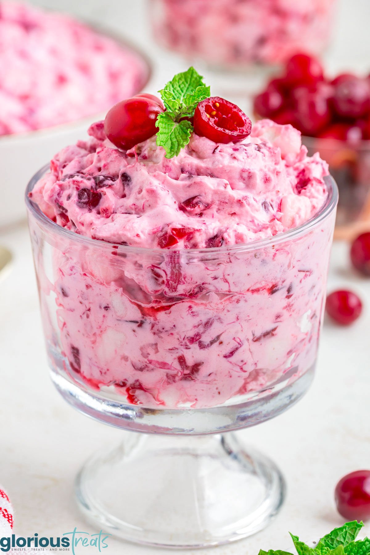 cranberry fluff dessert salad in glass individual serving cup topped with fresh cranberries and mint.