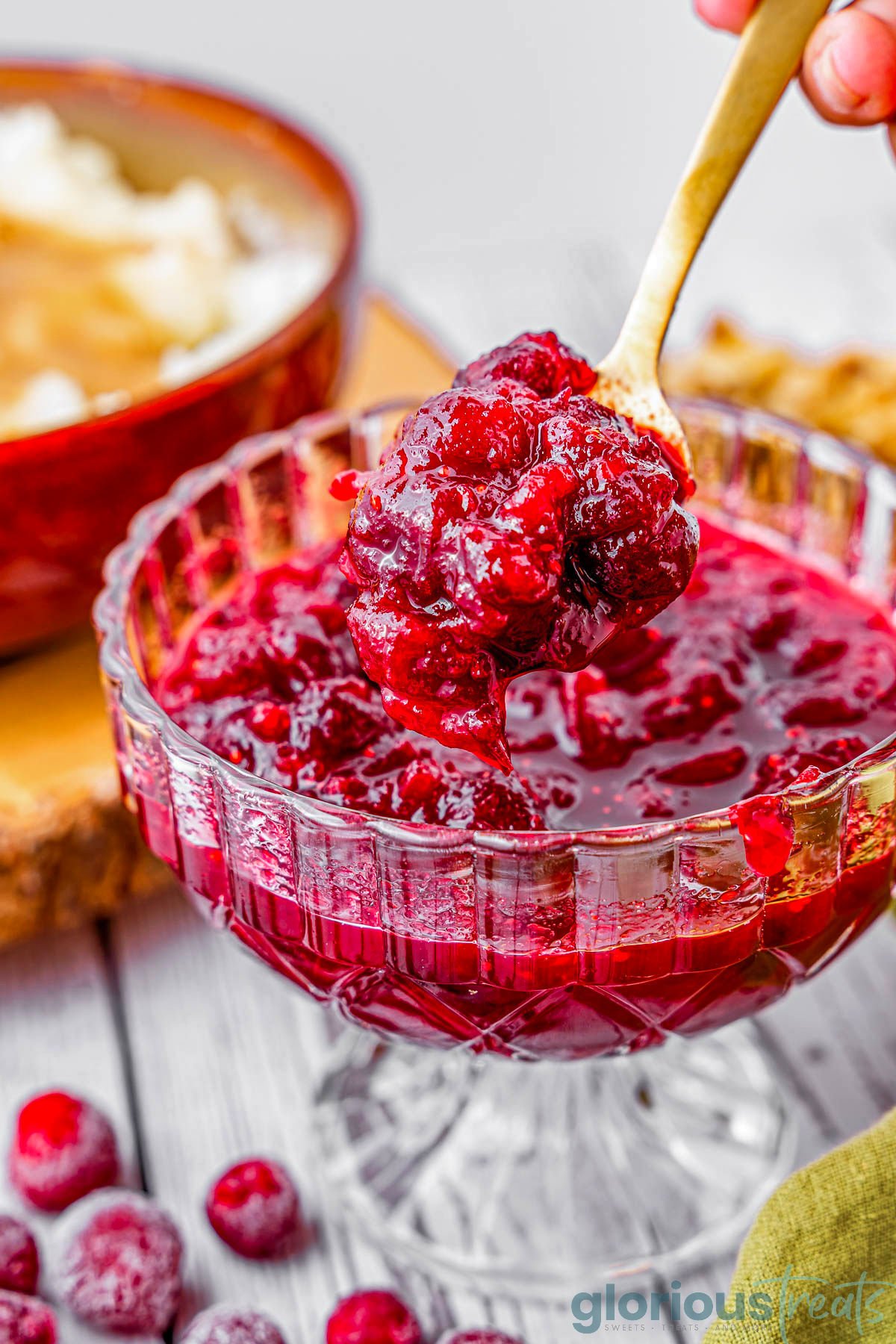 glass bowl filled with cranberry sauce with gold spoon lifting some out.