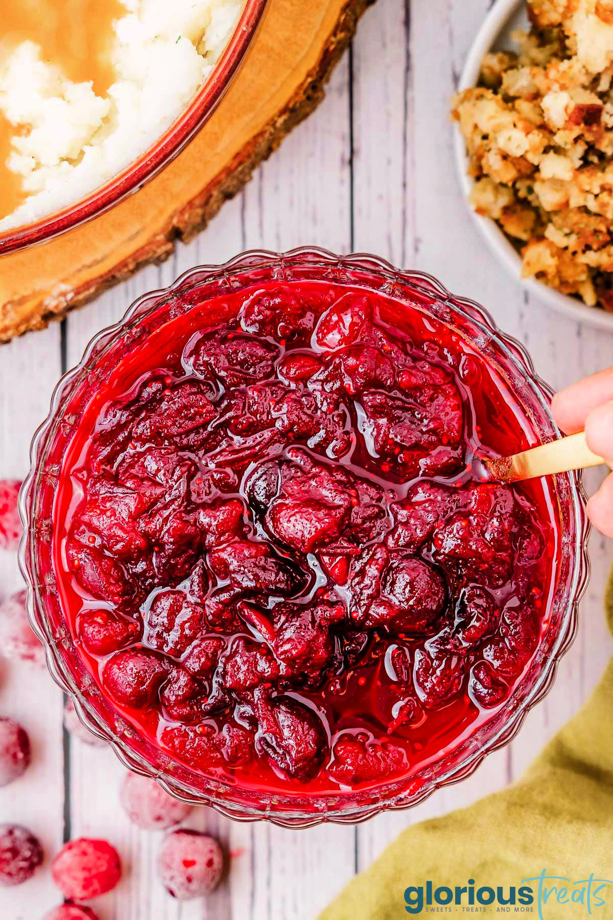 top down view of glass bowl of cranberry sauce with gold spoon in bowl.