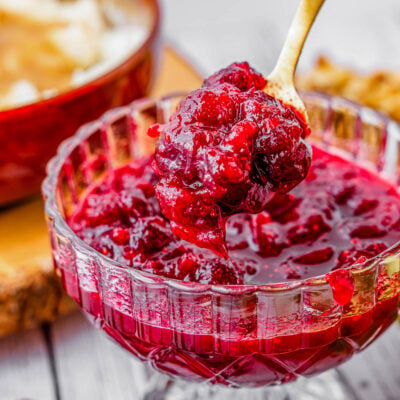 glass bowl filled with cranberry sauce with gold spoon lifting some out.