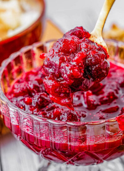 glass bowl filled with cranberry sauce with gold spoon lifting some out.