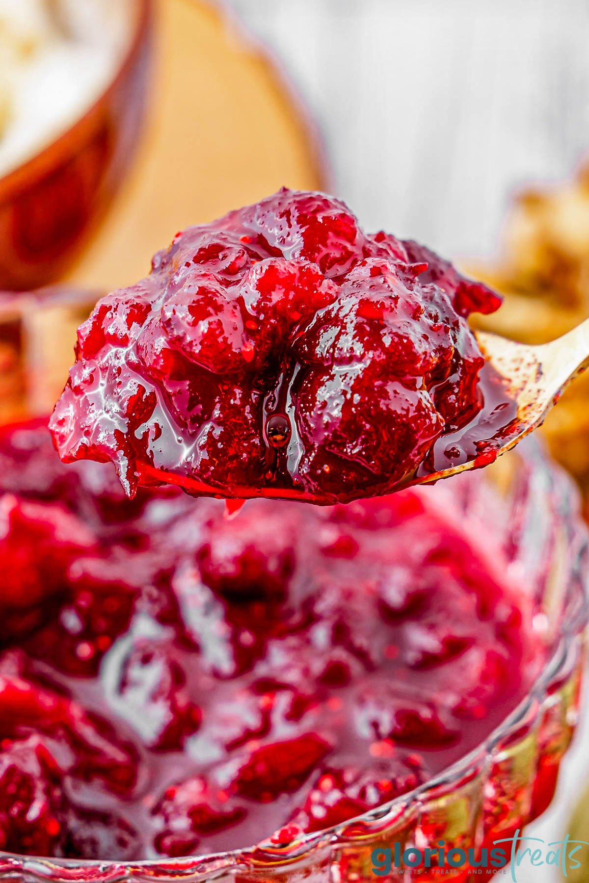 big spoon full of cranberry sauce being held over serving bowl.