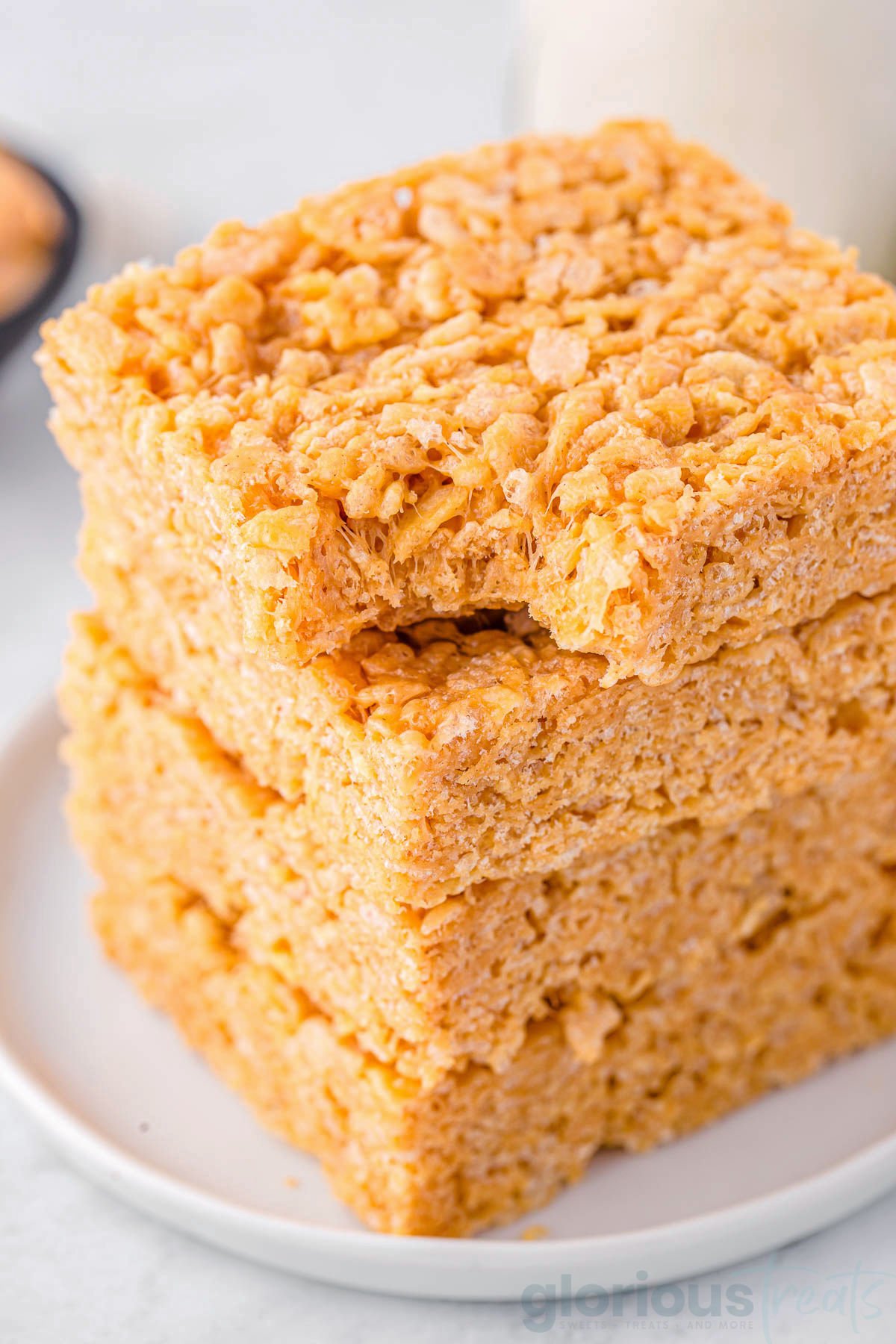 four peanut butter rice krispie treats stacked on a white round plate. the top treat has a bite taken out of it.