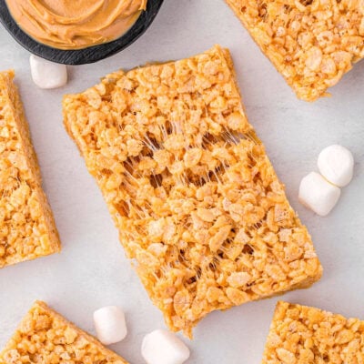 top down look at peanut butter rice krispies treats on a white surface with one treat pulled apart so you can see how gooey the treat is.