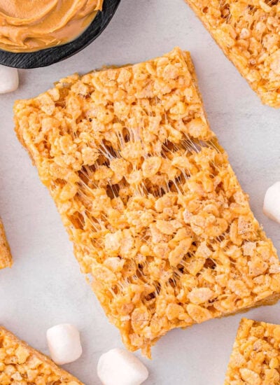 top down look at peanut butter rice krispies treats on a white surface with one treat pulled apart so you can see how gooey the treat is.