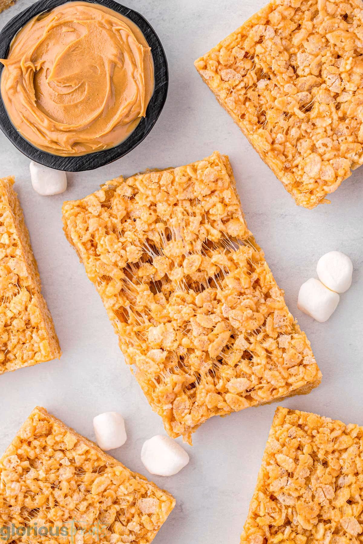 top down look at peanut butter rice krispies treats on a white surface with one treat pulled apart so you can see how gooey the treat is.