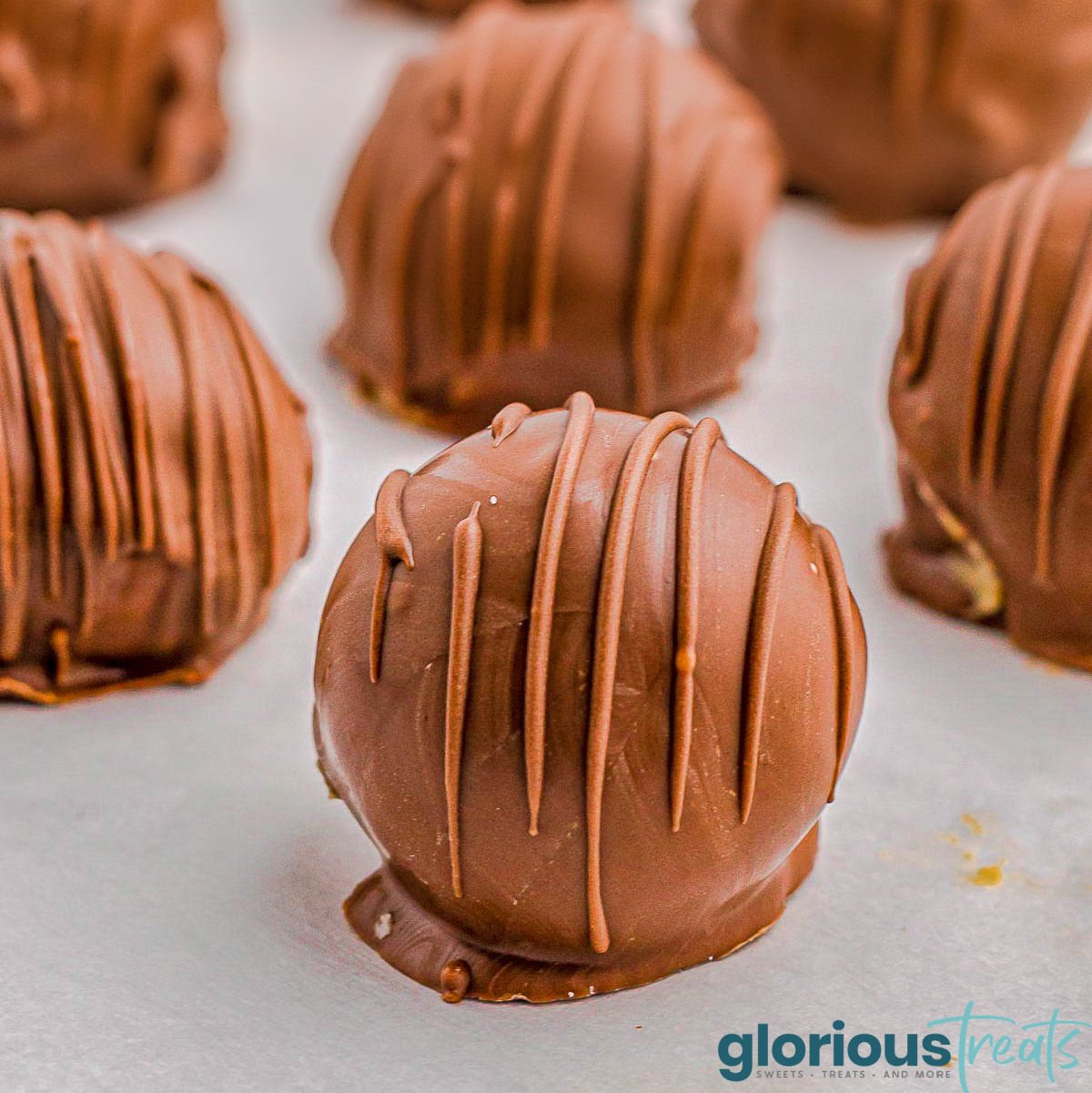 peanut butter balls sitting on parchment with chocolate drizzled on top.
