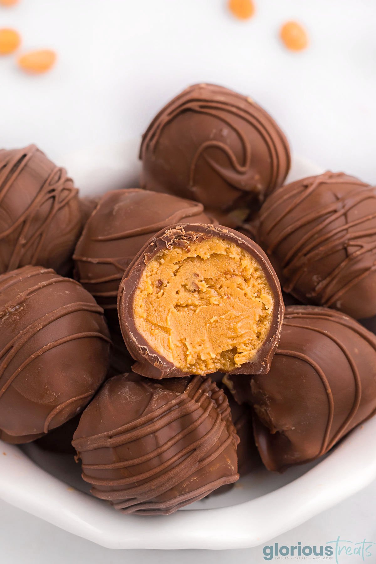 small white bowl with scalloped edges filled with homemade peanut butter balls recipe. top ball has been bitten in half.