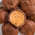 white round plate topped with a dozen or so peanut butter balls covered in chocolate. the top ball is split in half showing the creamy peanut butter filling.