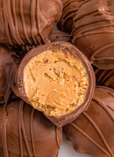 white round plate topped with a dozen or so peanut butter balls covered in chocolate. the top ball is split in half showing the creamy peanut butter filling.