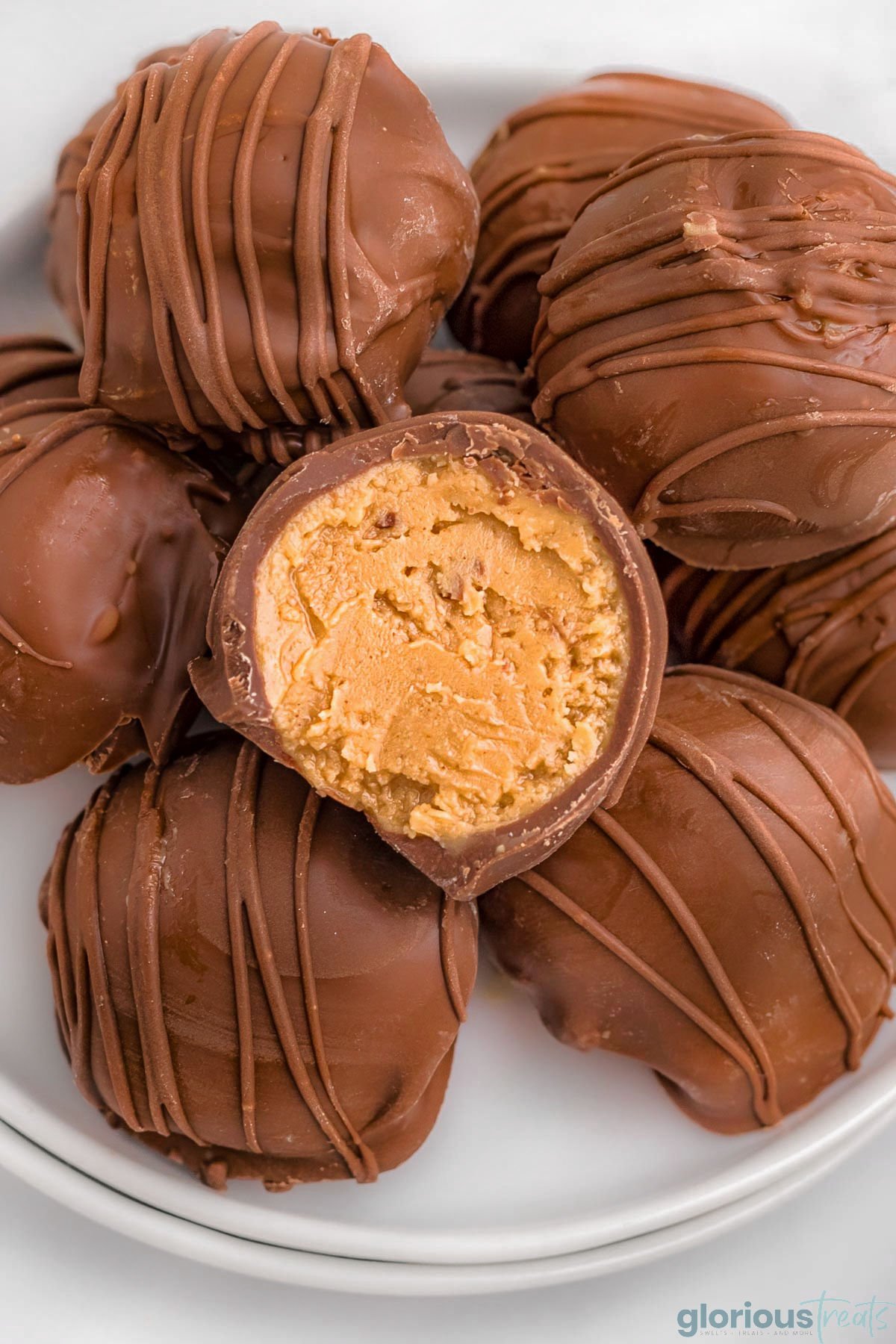 white round plate topped with a dozen or so peanut butter balls covered in chocolate. the top ball is split in half showing the creamy peanut butter filling.
