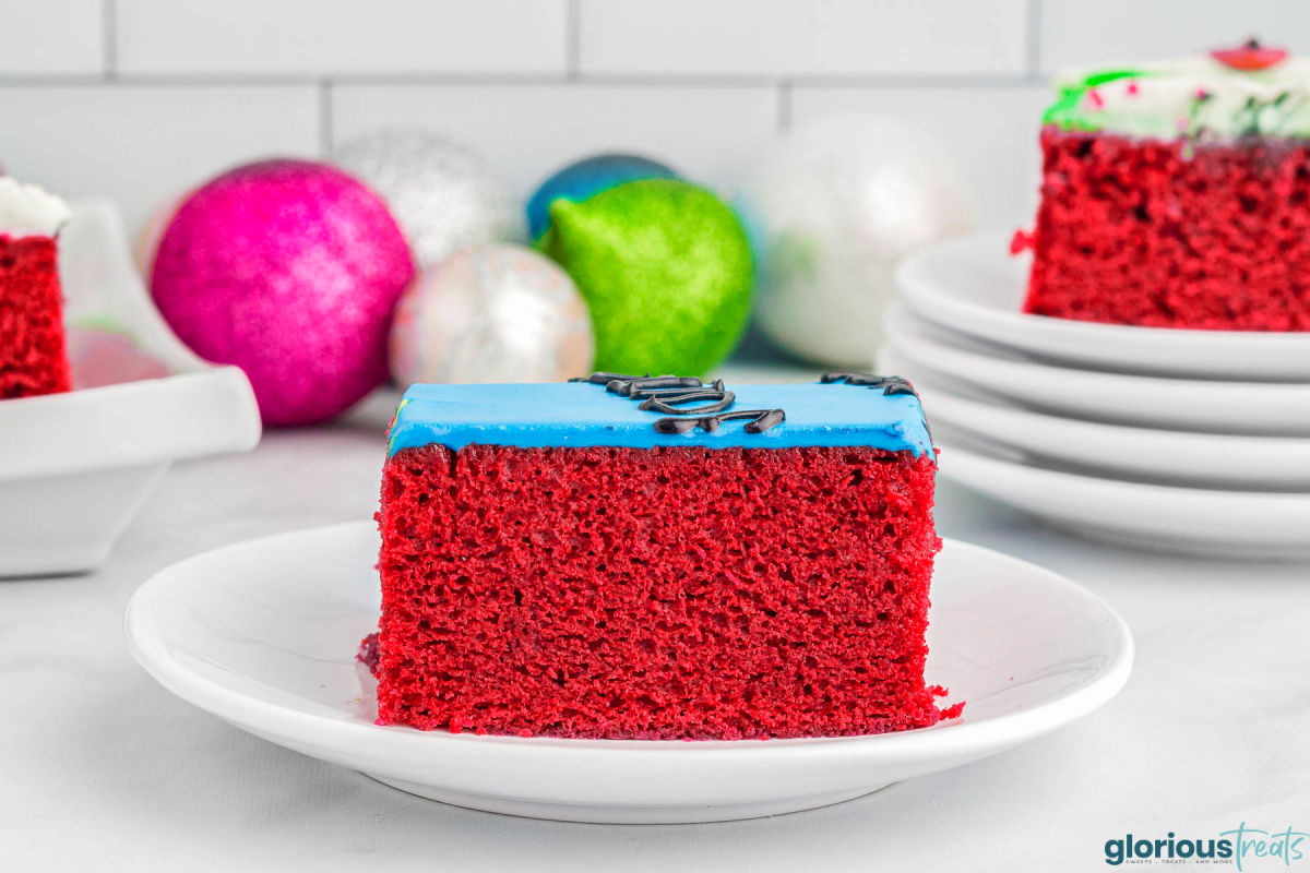 piece of red velvet cake frosted with cream cheese frosting and sitting on a round white plate.