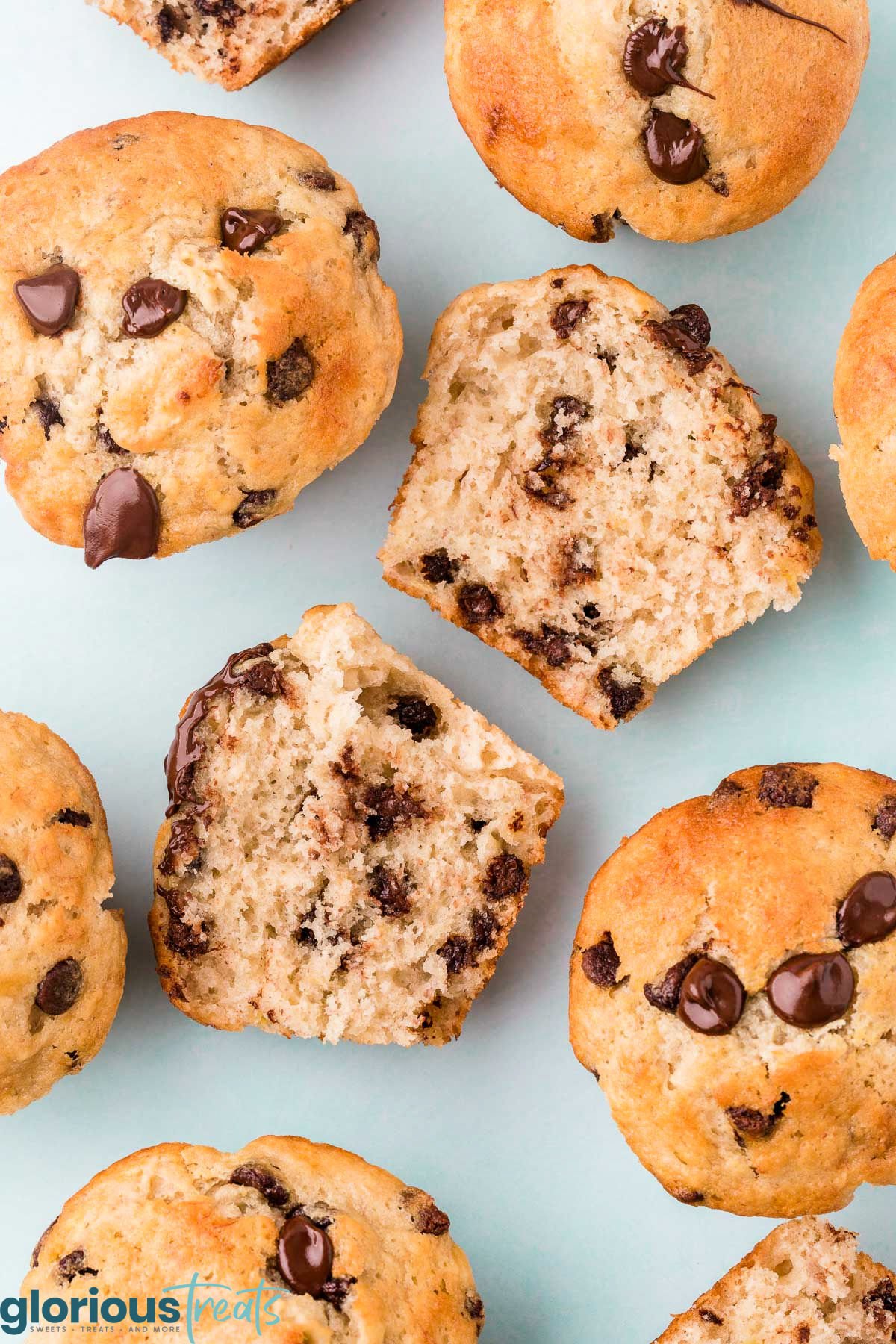 top down view of banana chocolate chip muffins with one muffin split in half showing the chocolate chips on the inside. light aqua background.