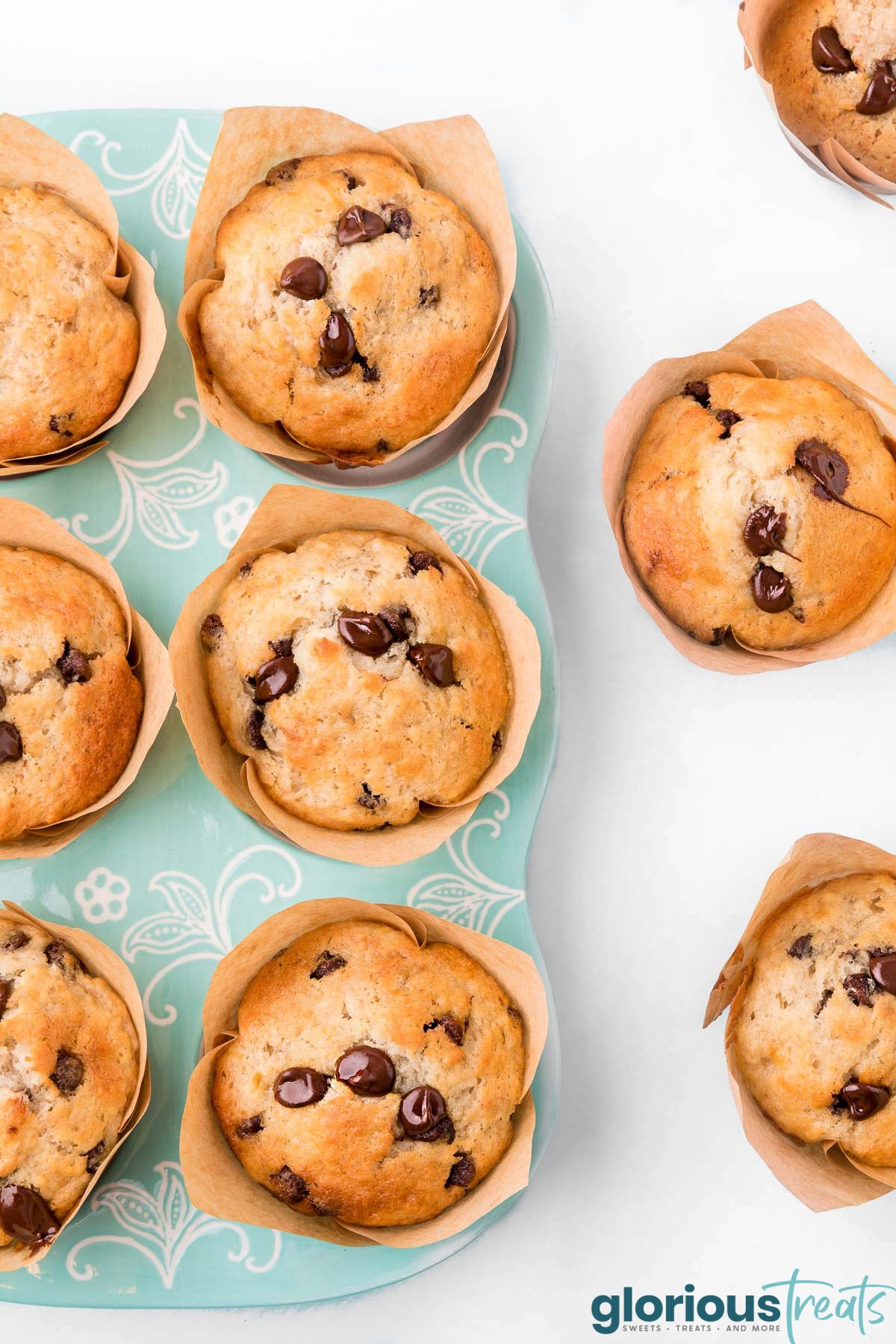 top down view of chocolate chip banana muffins in aqua muffin tin with three more muffins sitting next to the muffin tin.