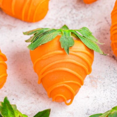 close up of strawberries dipping in orange candy to look like carrots.