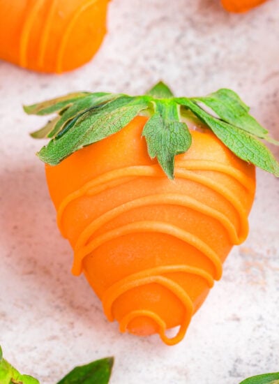 close up of strawberries dipping in orange candy to look like carrots.