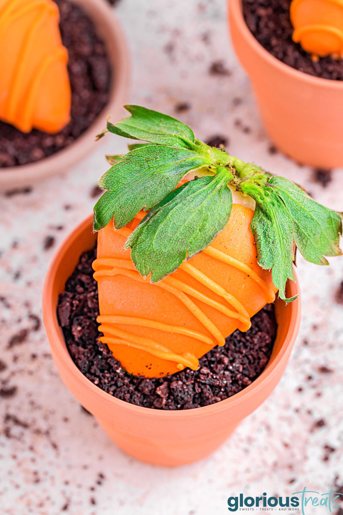 carrot strawberry in a clay pot filled with pudding and topped with crushed cookies.