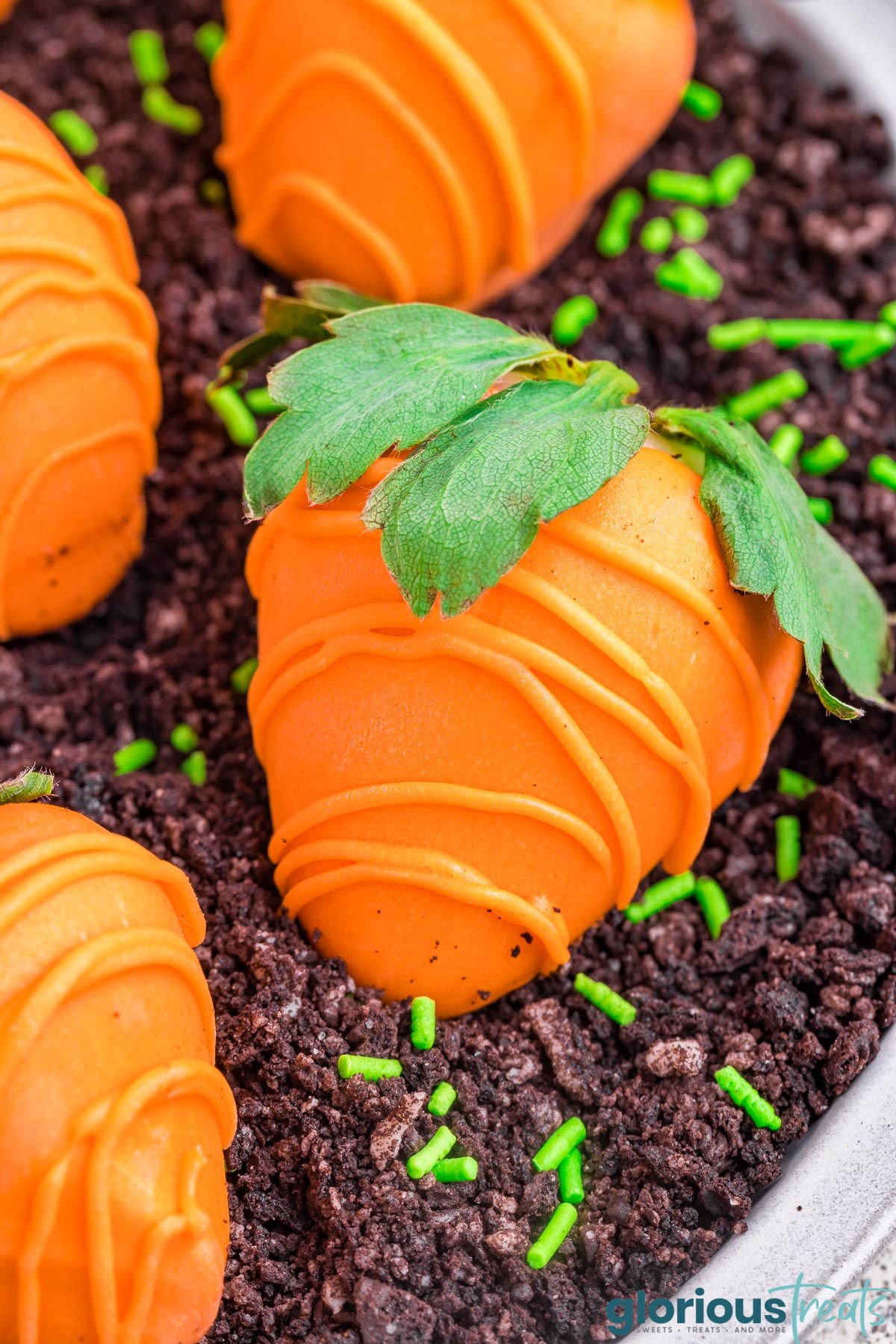 close up view of a round white plate that has been filled with crushed cookies to look like dirt and topped with candy dipped strawberries that look like carrots.