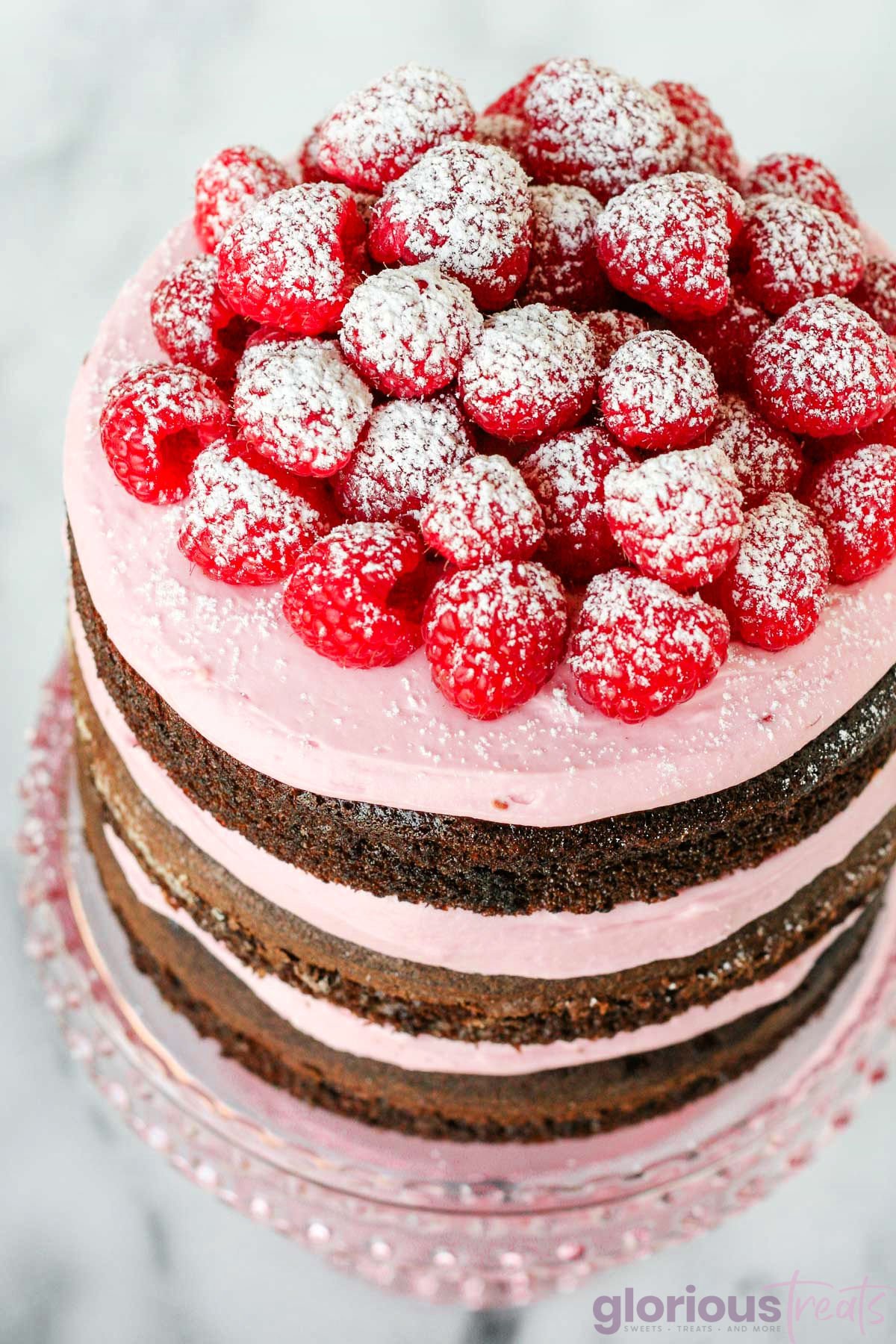 top down look at chocolate cake with raspberry buttercream and fresh raspberries. the cake is naked with just layers showing.