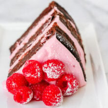 Generous slice of chocolate raspberry cake topped with fresh raspberries and sitting on a white plate.