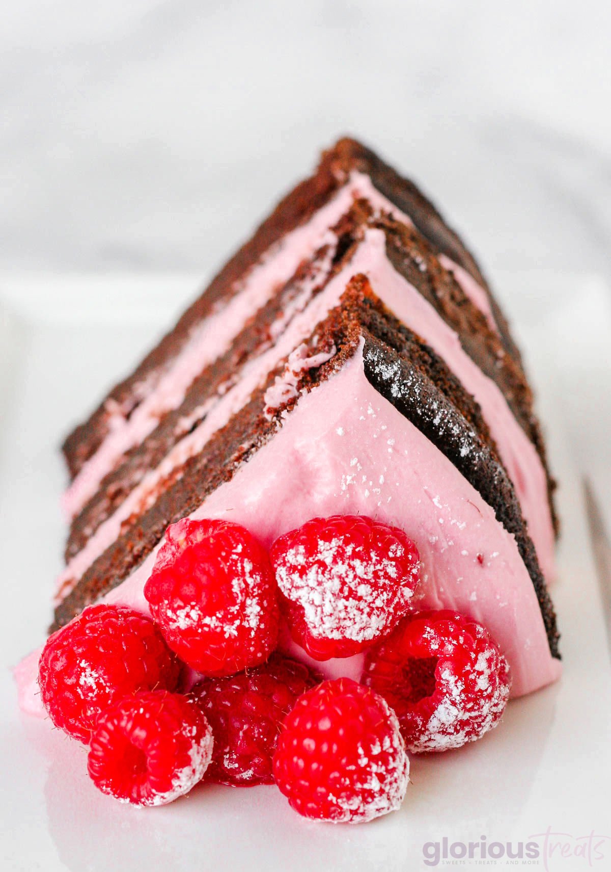 Generous slice of chocolate raspberry cake topped with fresh raspberries and sitting on a white plate.