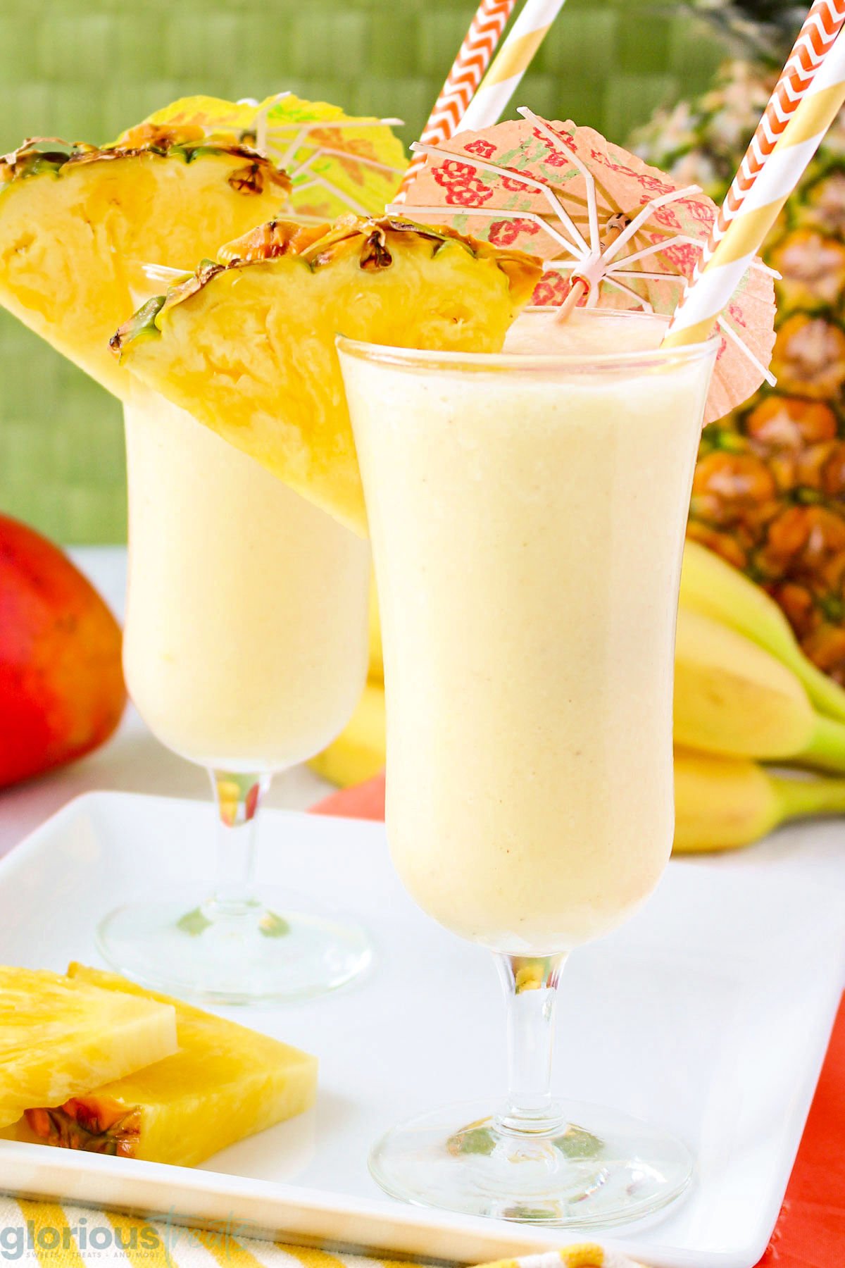 two tropical fruit smoothies garnished with pineapple wedges and small paper umbrellas along with paper straws.