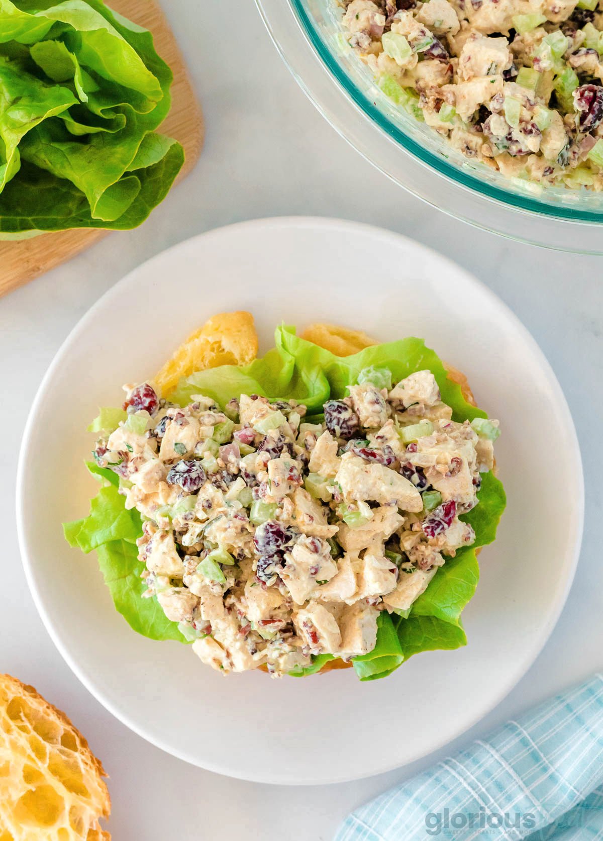 top down view of chicken salad layered with butter lettuce on one half of a large croissant sitting on a round white plate.