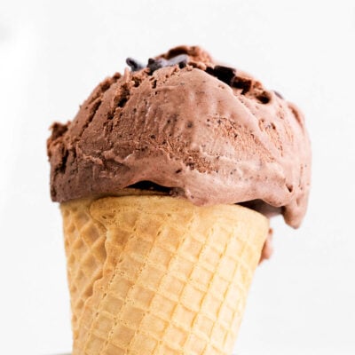 A side view of a scoop of chocolate ice cream on a cone in a glass jar.