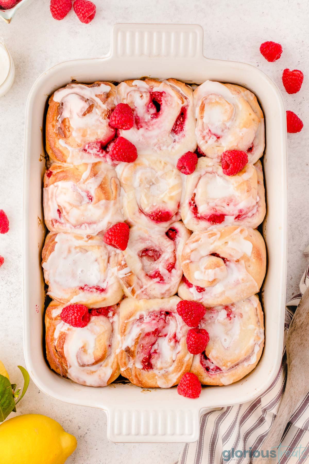 a top down shot of a pan of raspberry sweet rolls on a white surface.