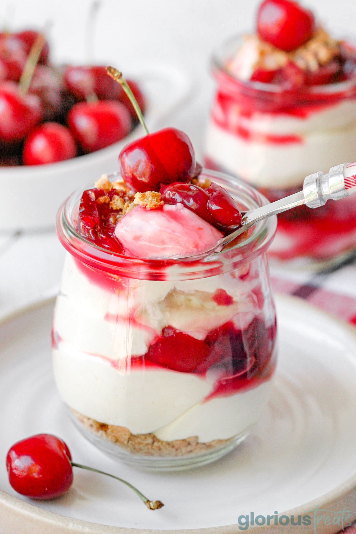 a small glass container full of cherry cheesecake with a spoon lifting up a bite