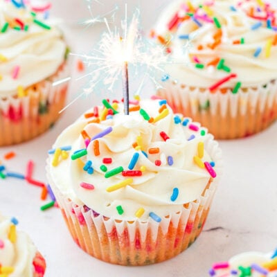 Birthday cupcakes on a white surface with a candle in one of them.