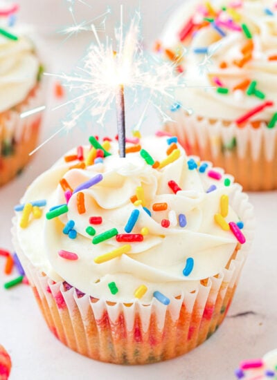 Birthday cupcakes on a white surface with a candle in one of them.