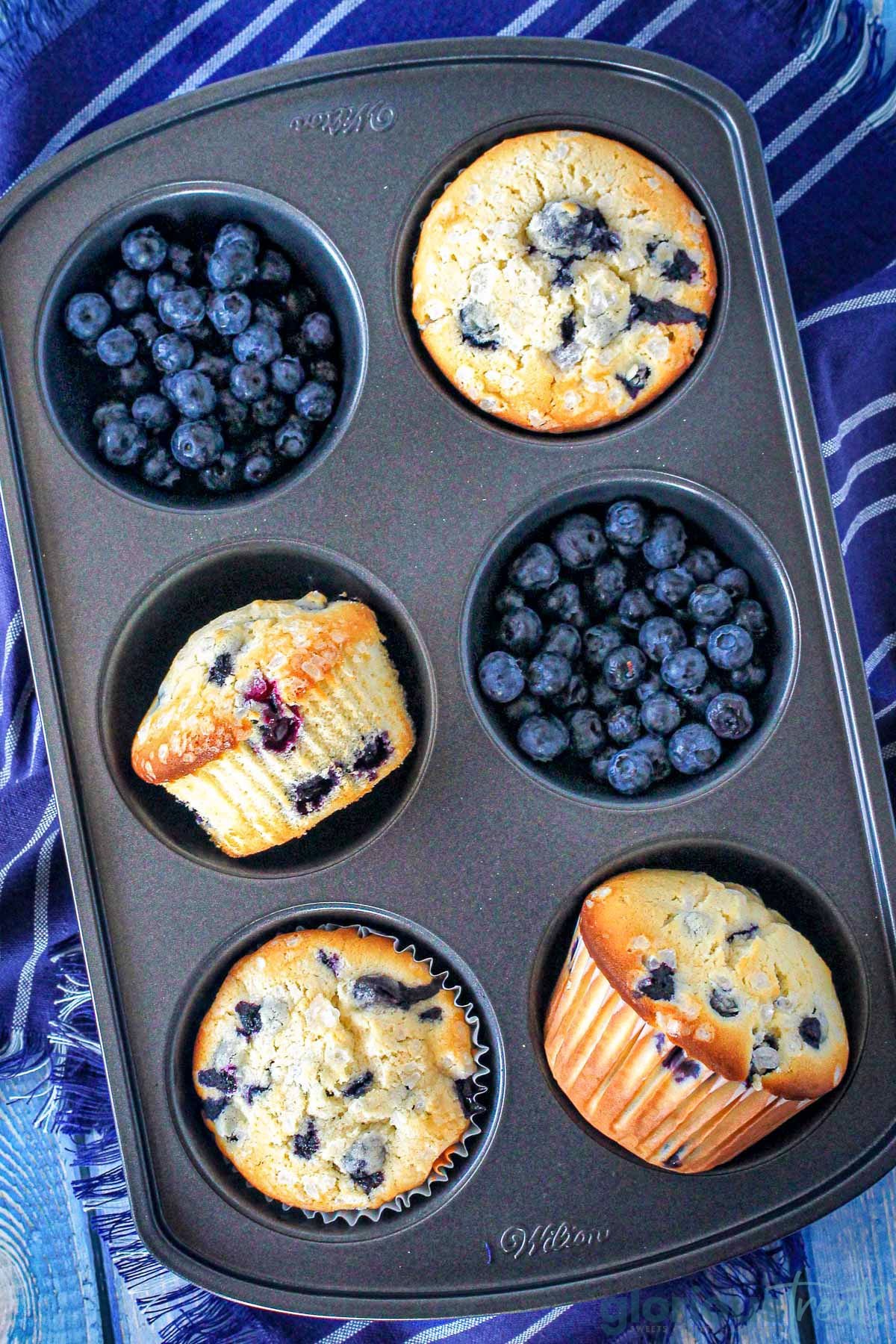 Blueberries and blueberry muffins in a muffin tin.